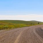 A gravel road through Alberta farmland and hills.