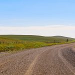 A gravel road through Alberta farmland and hills.